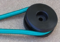 Une poulie en plastique noir traversée par une corde turquoise, posée sur une surface grise.