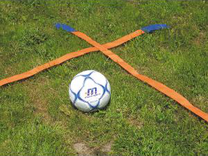 Un ballon de football sur une pelouse verte, entouré de bandes de marquage orange.