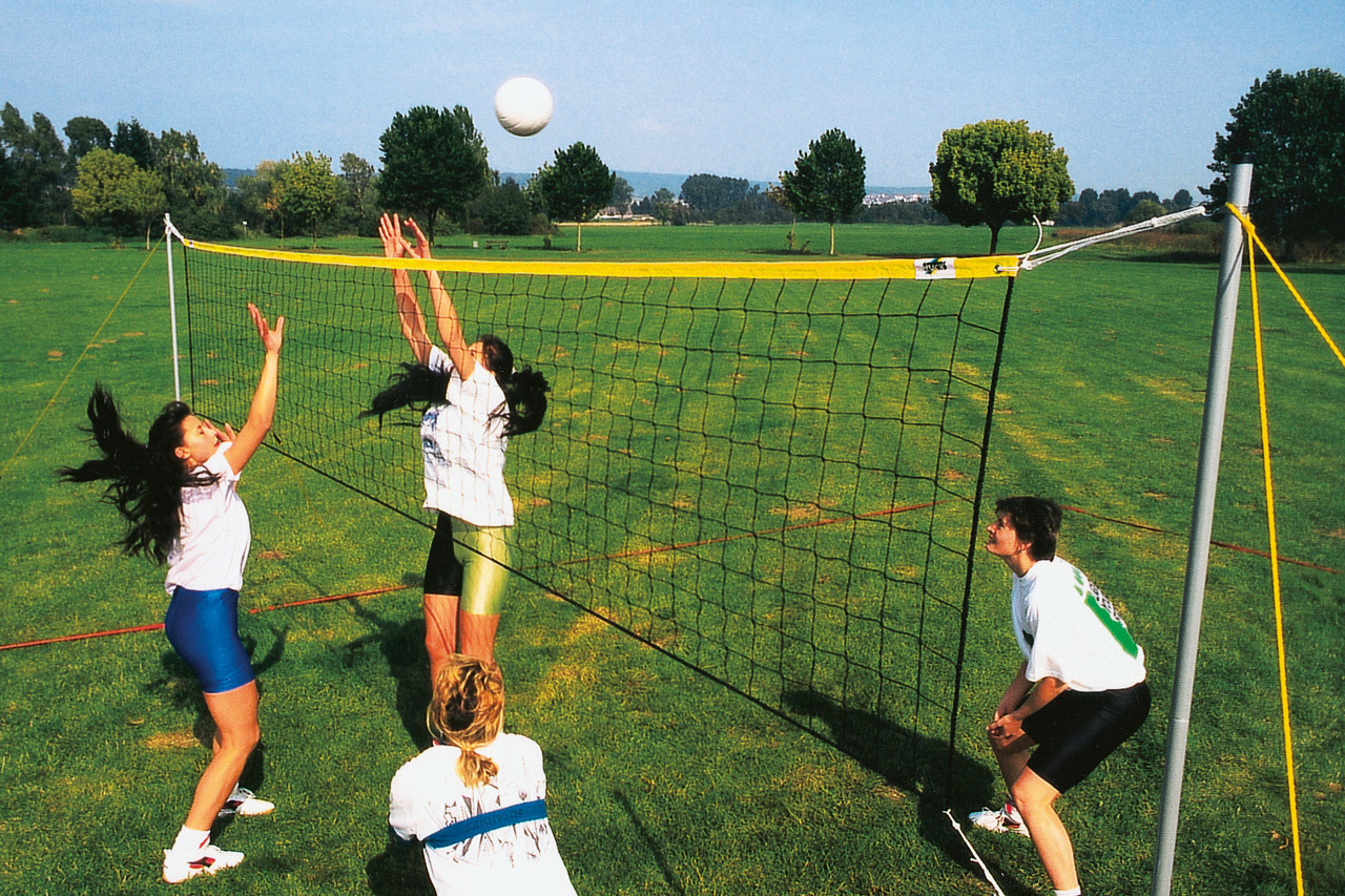 Vier Personen spielen Volleyball auf einem grünen Feld unter klarem Himmel.