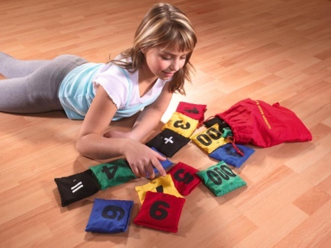 Une fillette est allongée sur le sol et joue avec des sacs en tissu numérotés et colorés. Les sacs sont étalés devant elle.
