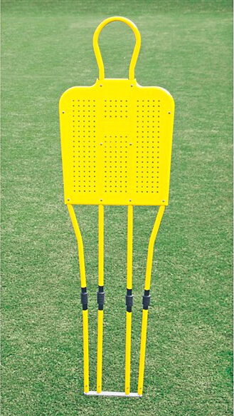 Un mannequin d'entraînement de football jaune est placé sur un terrain en gazon vert. Le mannequin a un arc de cercle en haut et se compose de plusieurs barres.