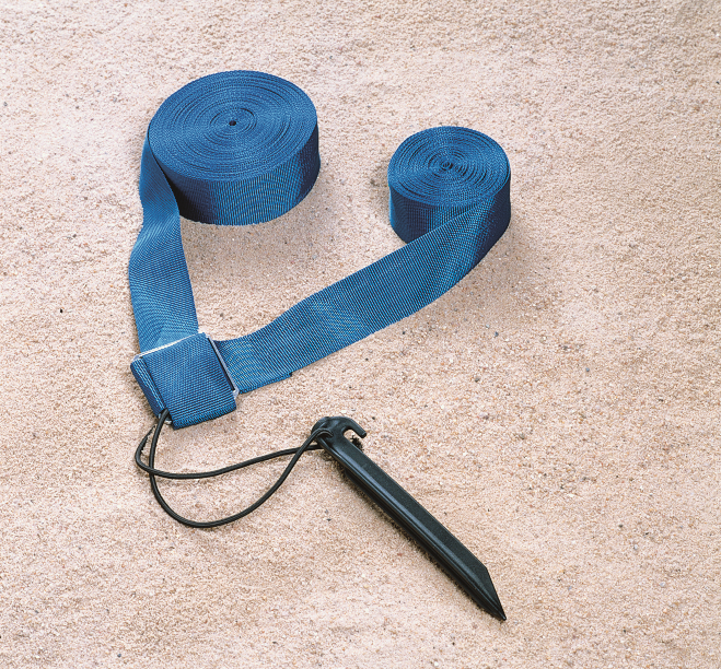 Sangle de fixation bleue sur sol sablonneux avec piquet de terre noir.
