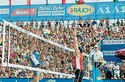 Volleyballspieler beim Beachvolleyball-Turnier in Aktion, umgeben von einer großen Menschenmenge auf den Tribünen